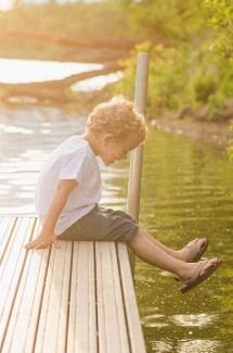 Junge sitzt am Steg und schaut ins Wasser